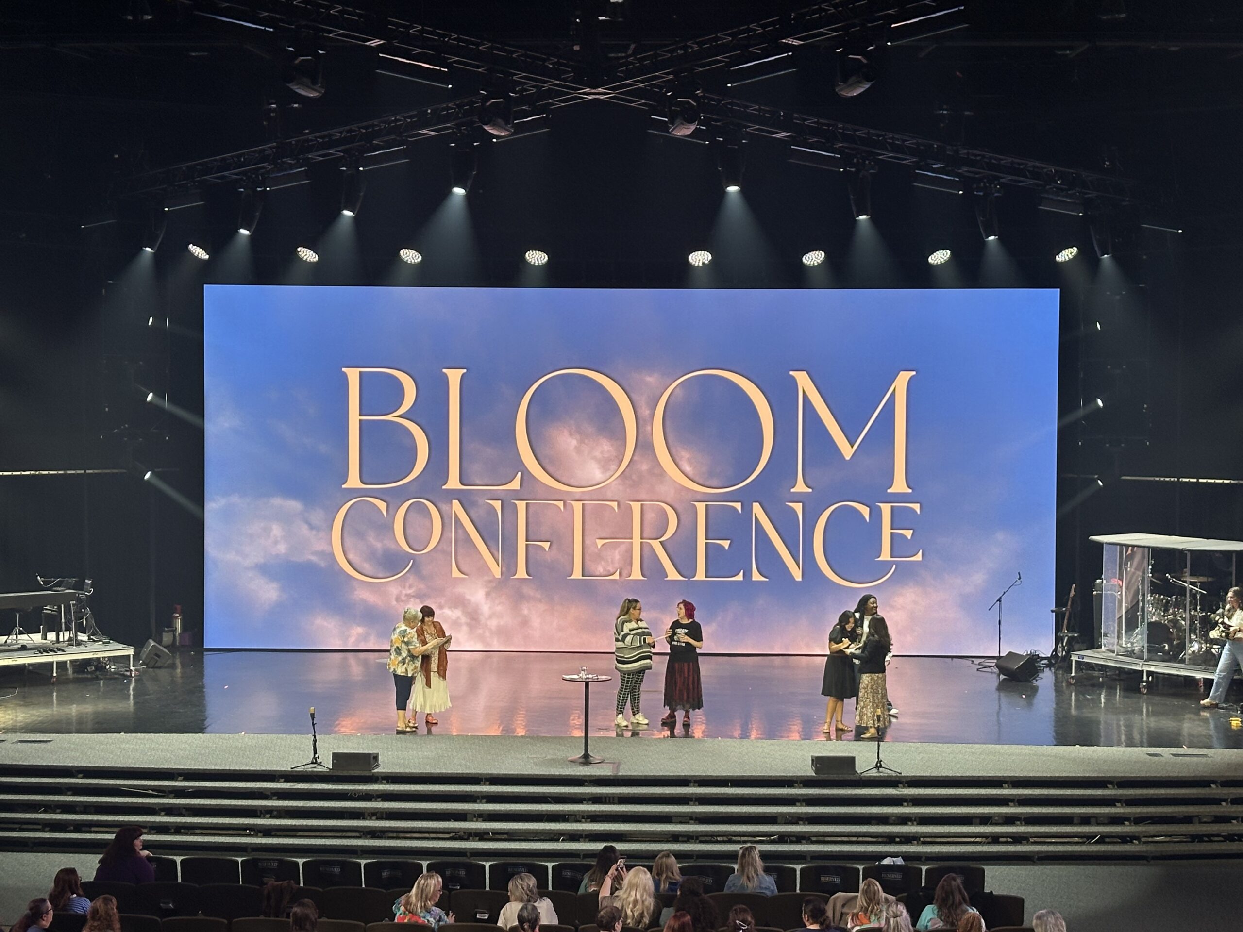 Ministry leaders praying and encouraging women on stage during Bloom Conference in North Texas.
