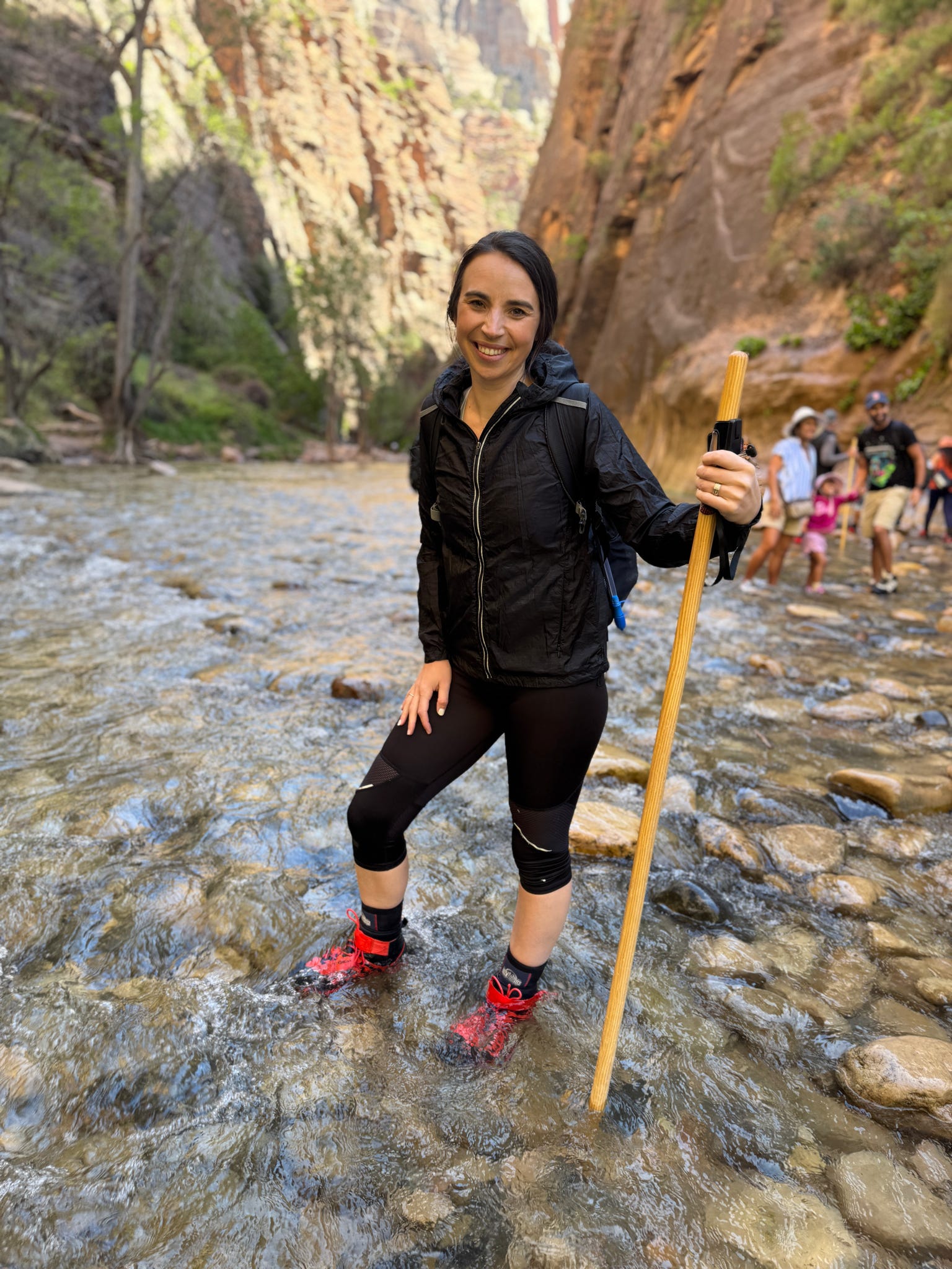 Woman hiking through the Virgin River with a walking stick during The Narrows hike in Zion National Park.