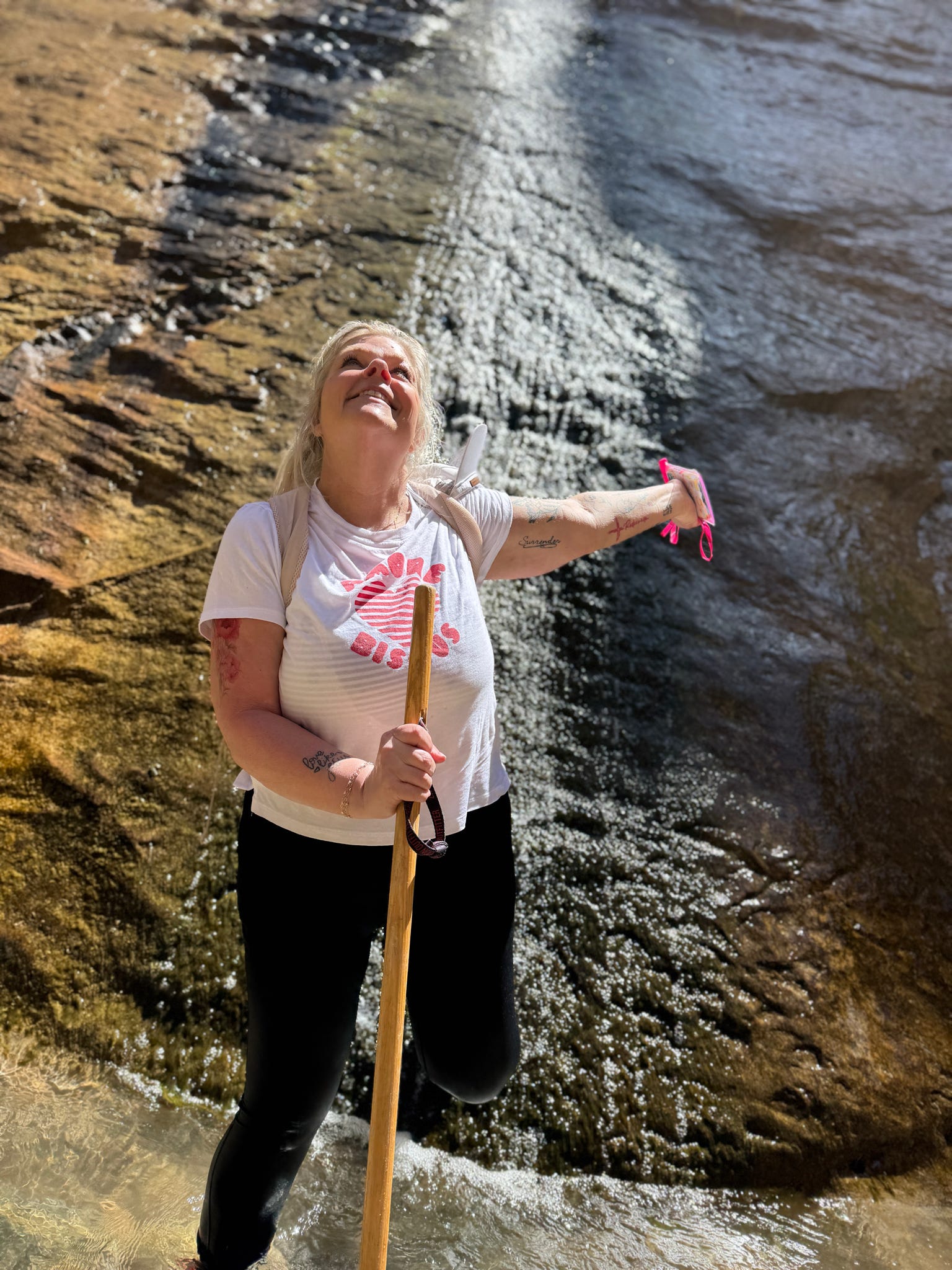 Woman standing beneath a waterfall in Zion National Park looking upward in wonder.