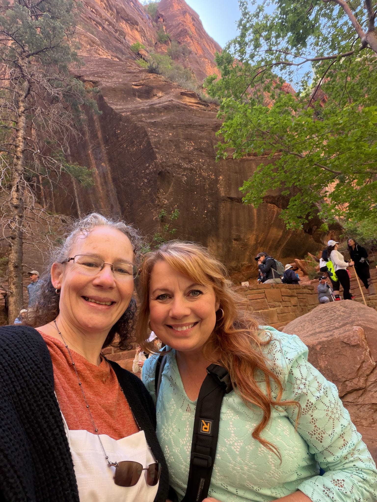 Two women smiling together with Zion Canyon cliffs in the background.