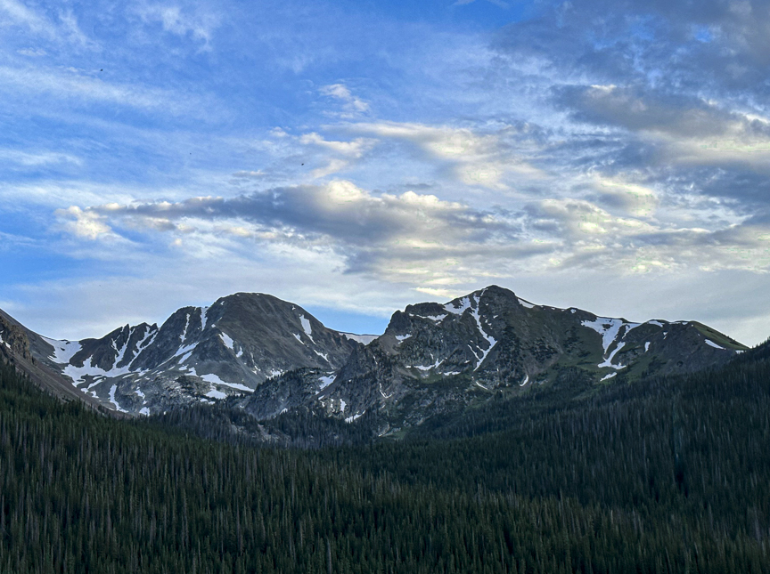 Rugged Colorado mountain peaks with patches of snow rising above a dense evergreen forest