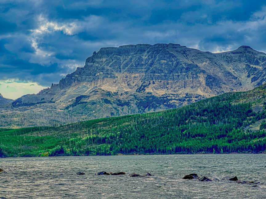 Massive layered mountain rising above Saint Mary Lake beneath dark storm clouds in Glacier National Park