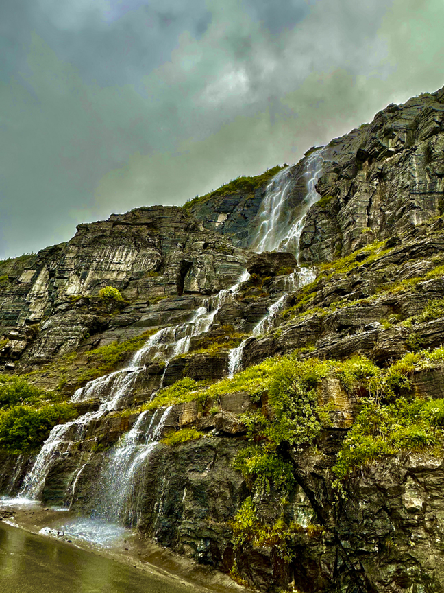 Tall waterfall cascading down a layered rocky cliff beside the Going-to-the-Sun Road in Glacier National Park